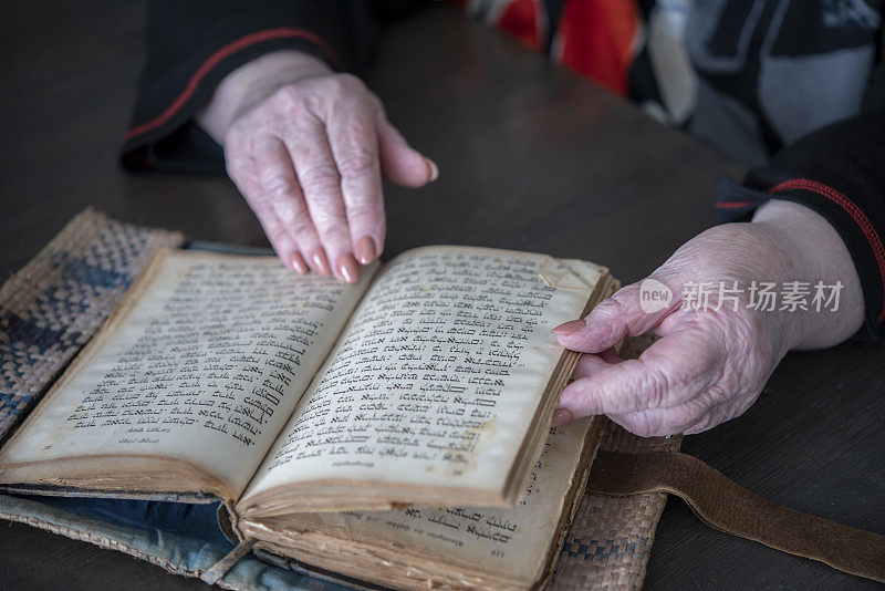 Mature woman reading ancient analogue book in Hebrew.